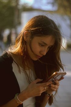 A young woman focuses on her smartphone while walking outdoors during the day.