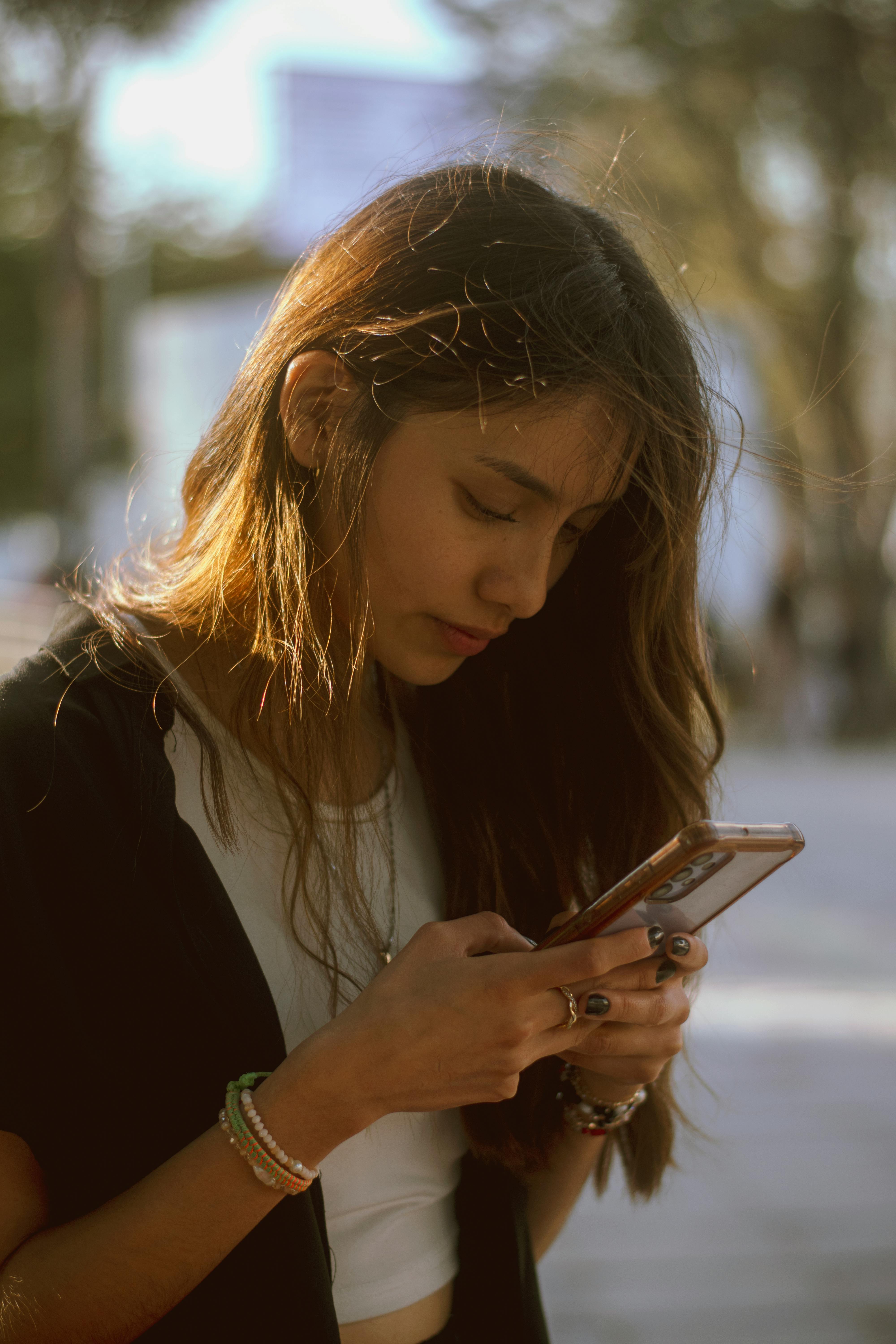 Young woman focused on her smartphone outdoors in natural lighting.