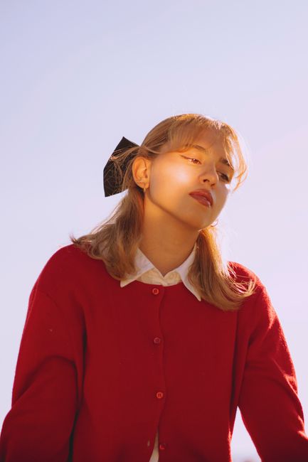 Portrait of a young woman in a red sweater with sunlight on her face, creating a serene atmosphere.