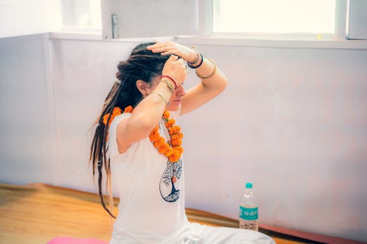 A woman engages in meditation, wearing a garland, indoors with soft lighting.