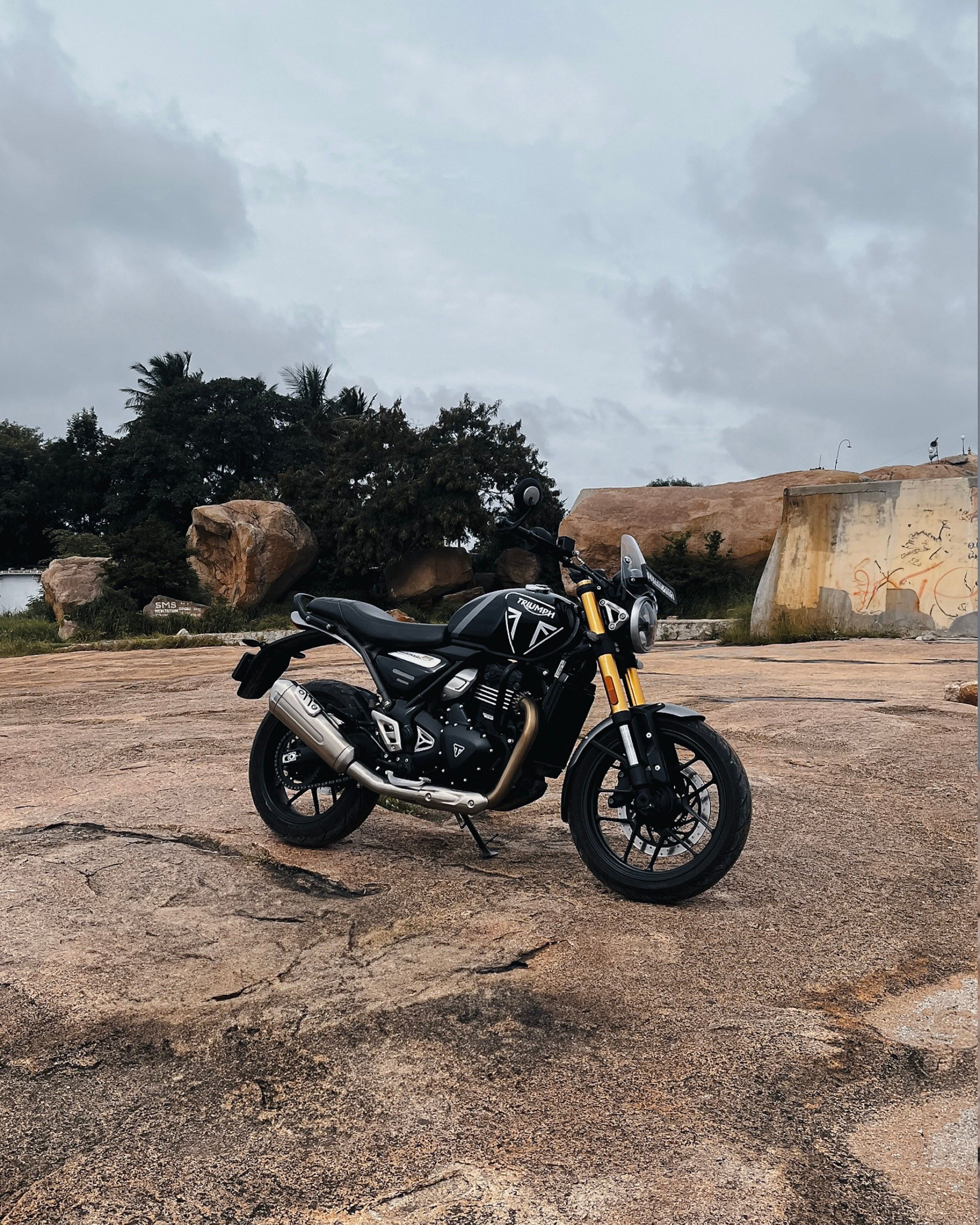 A sleek black motorcycle parked on rugged rocks with a cloudy sky backdrop, perfect for travel enthusiasts.