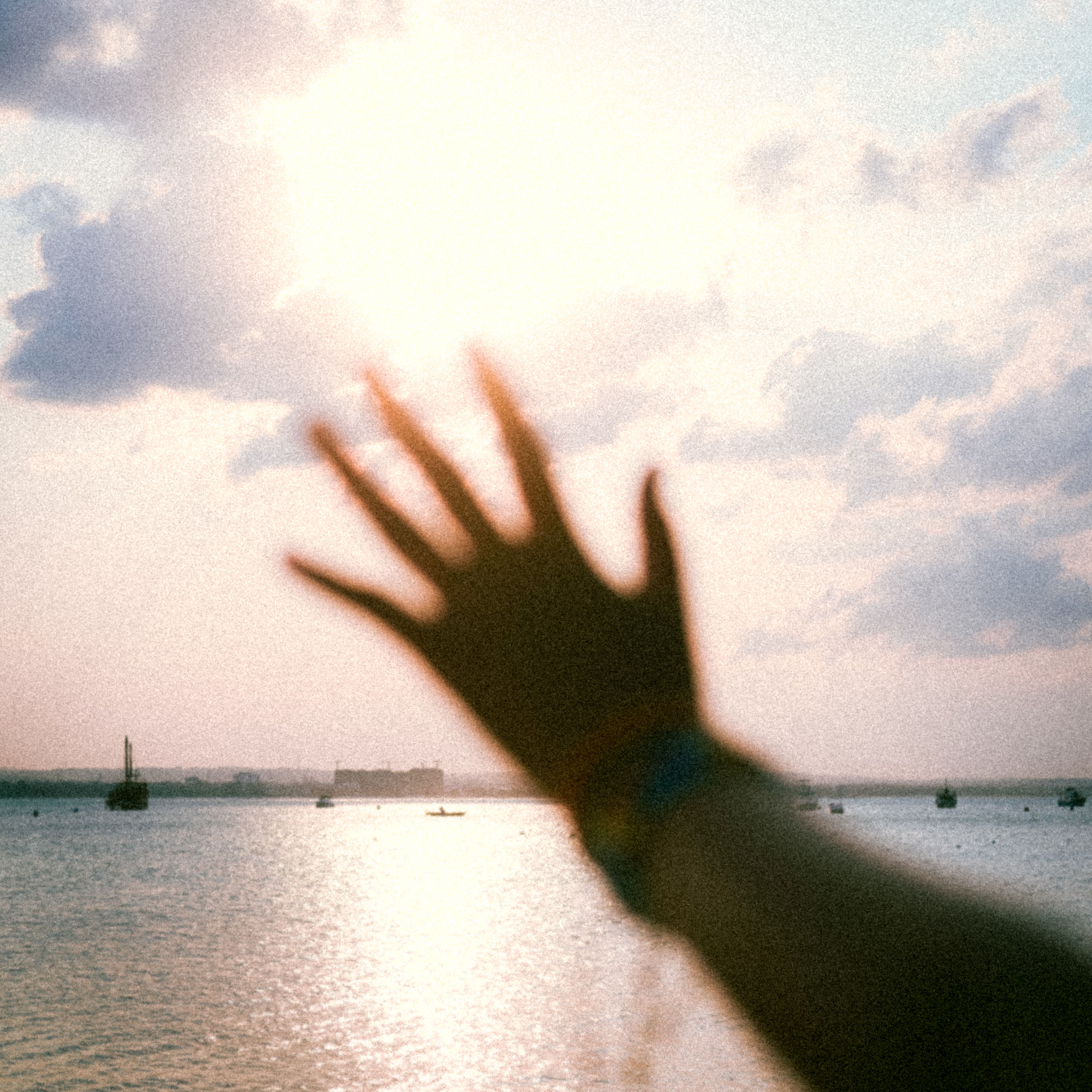 A silhouette of a hand reaching out towards the sun over a tranquil ocean.