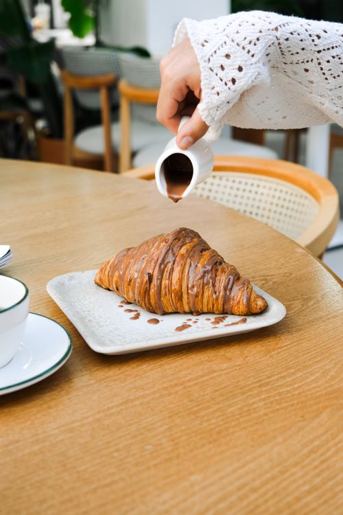 Free A hand drizzling chocolate over a croissant in a cozy Adana cafe setting. Stock Photo