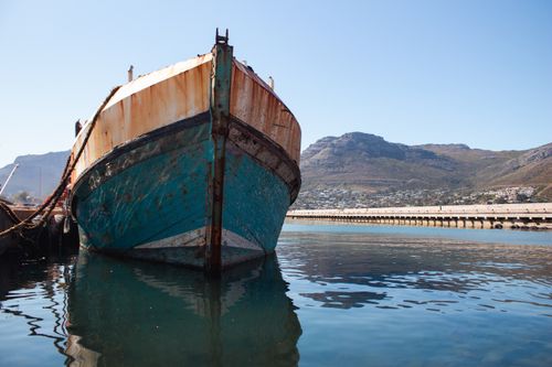 Free A rustic boat rests peacefully in a tranquil harbor, framed by scenic mountains under clear blue skies. Stock Photo