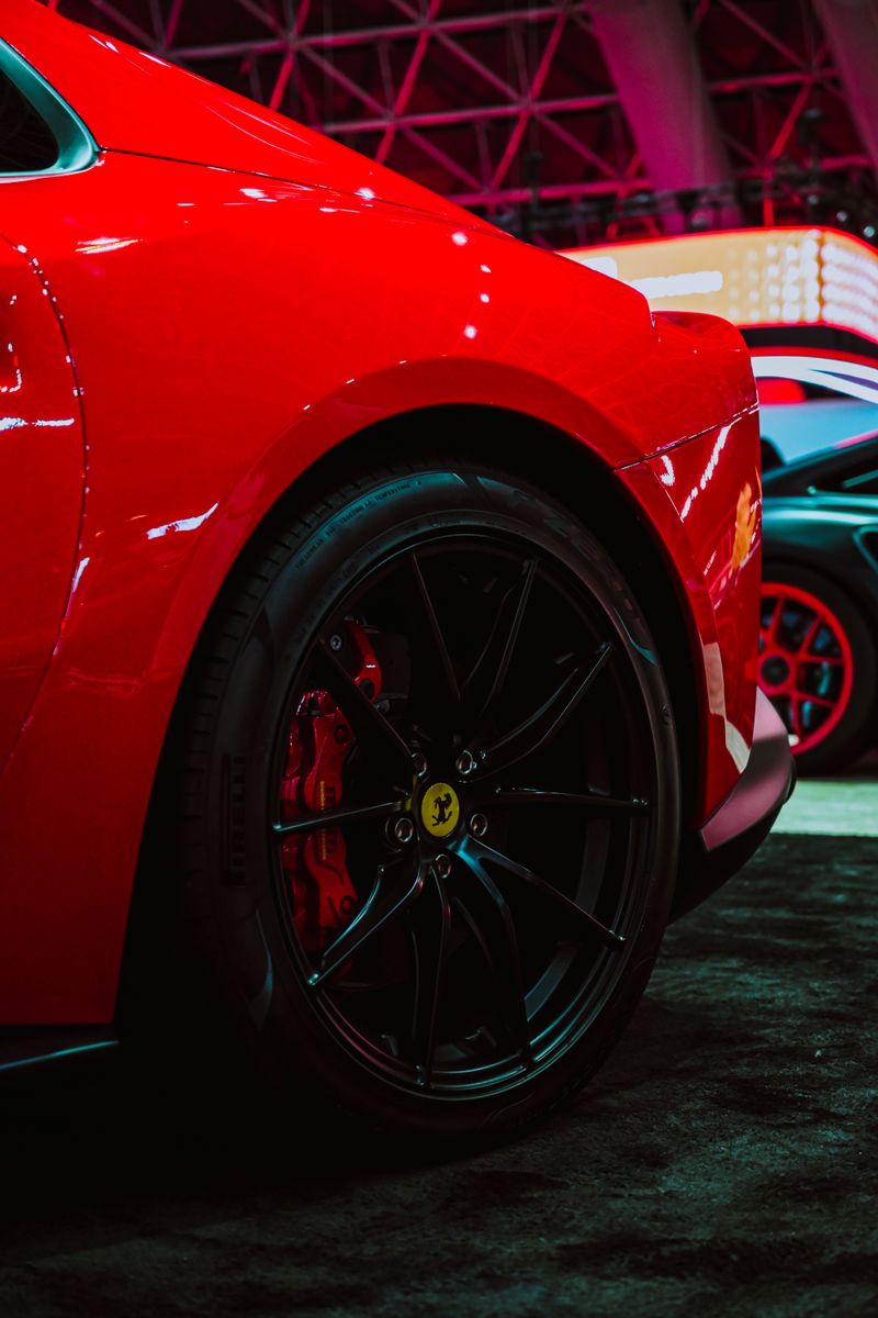 Close-up of a sports car's rear and wheel, showcasing a sleek red design with black alloys.