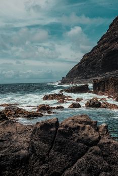 在多云的天空下，海浪拍打着崎岖的岩石海岸线