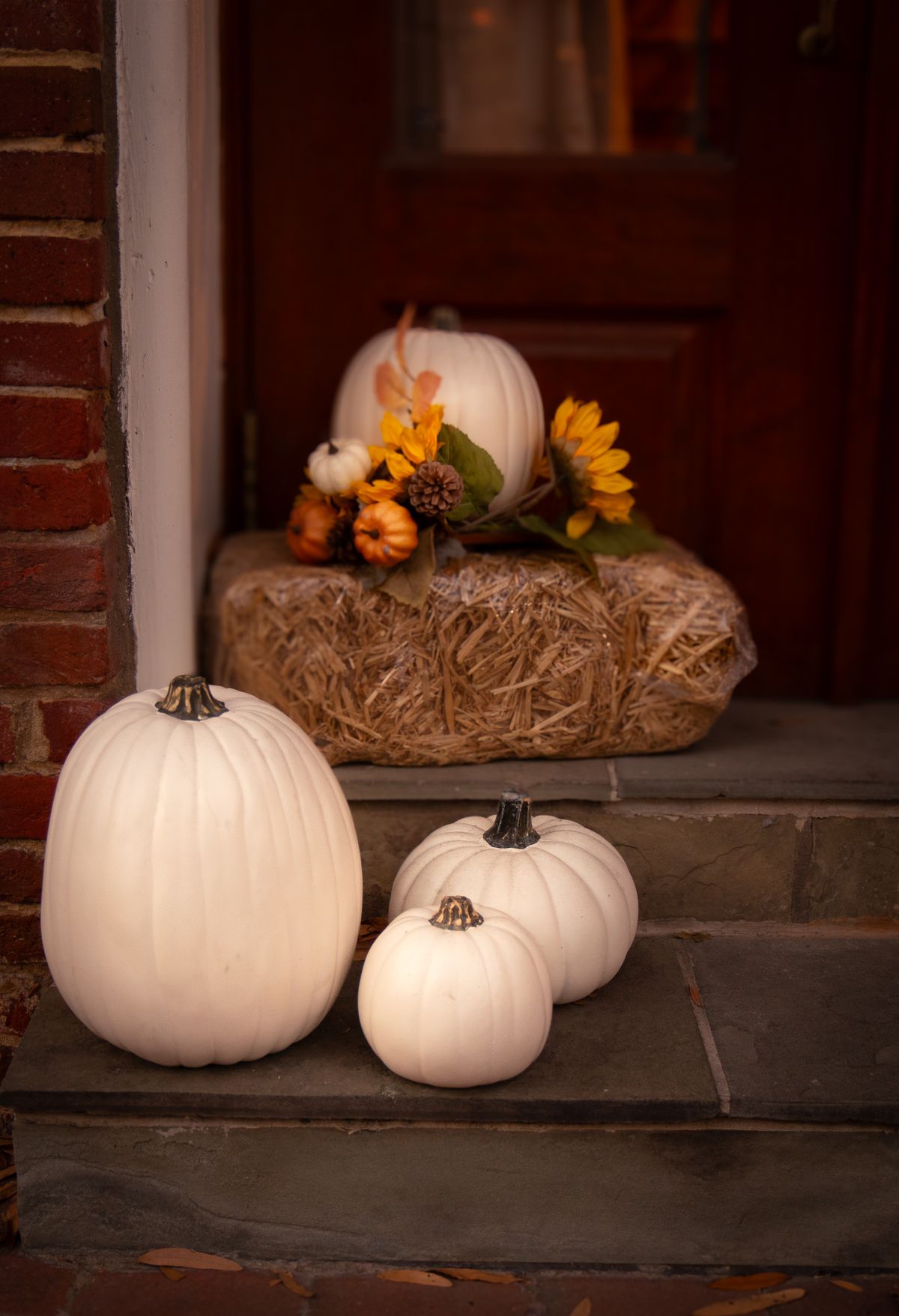 Airy fall porch with white pumpkins and an autumn floral arrangement on a hay bale