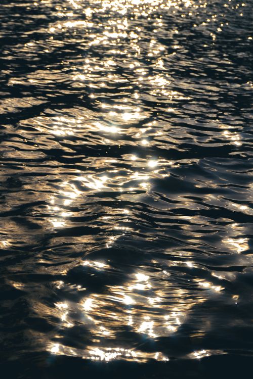 Free Sunset reflections casting warm tones on rippled water surface, creating dynamic textures. Stock Photo
