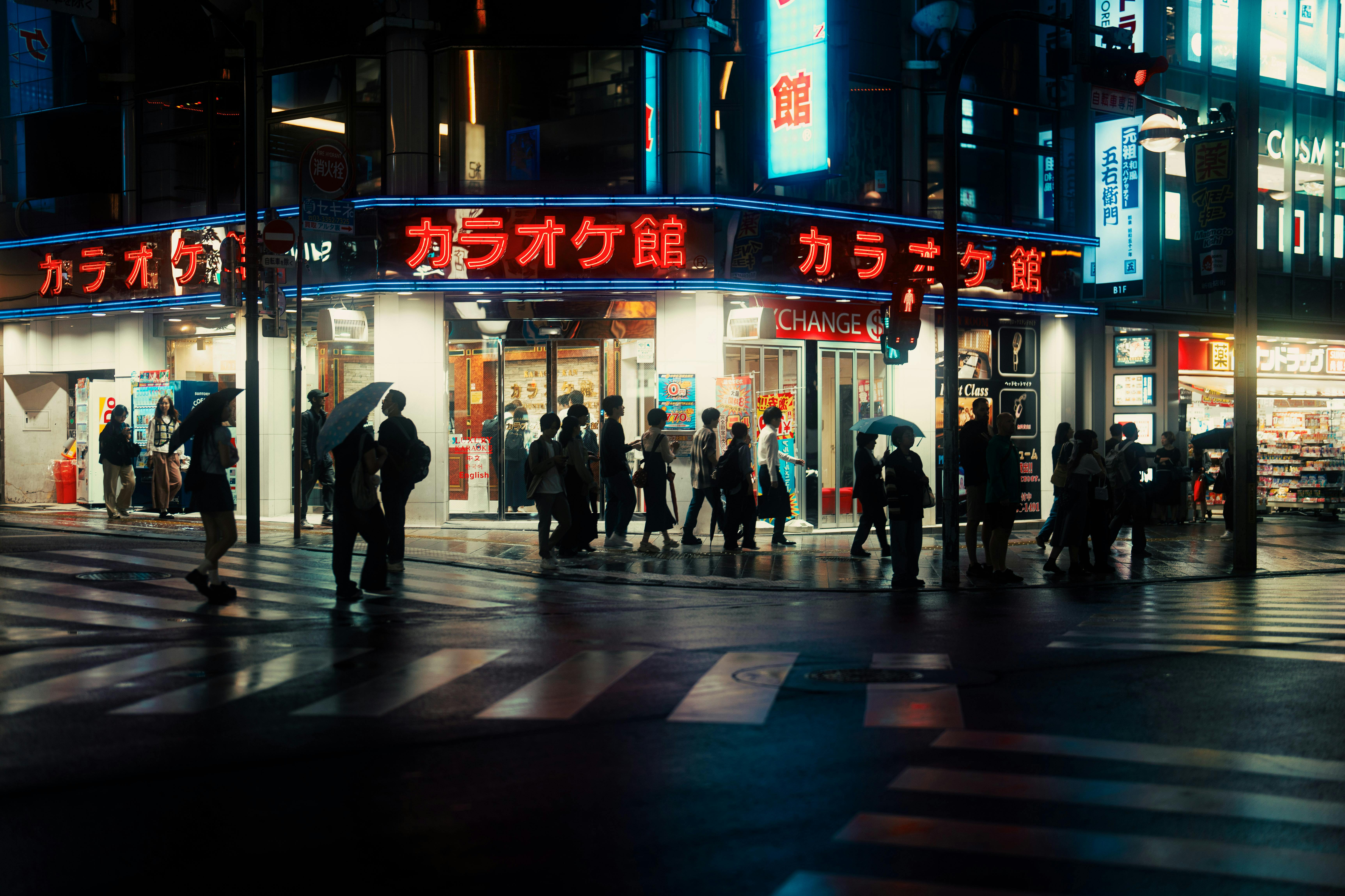 Bustling Tokyo street at night with neon lights and people under umbrellas.