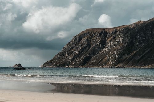Free Scenic view of towering sea cliffs by a sandy beach under a moody cloudy sky. Stock Photo