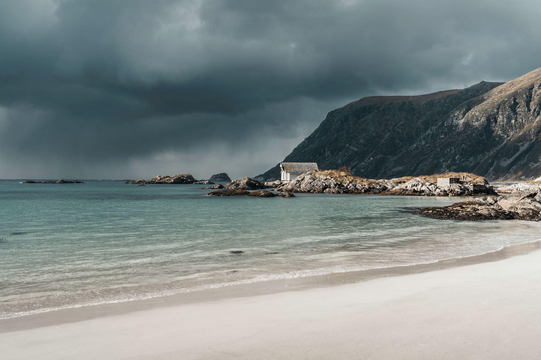 Breathtaking view of Norwegian sea cliffs and a white sand beach under a dramatic cloudy sky.