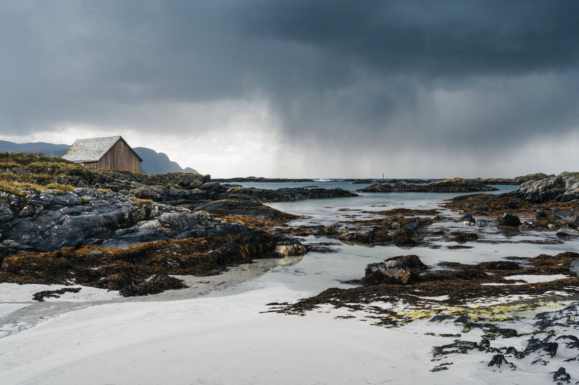 Scenic view of a beach hut near rocky cliffs under a stormy sky in Norway.
