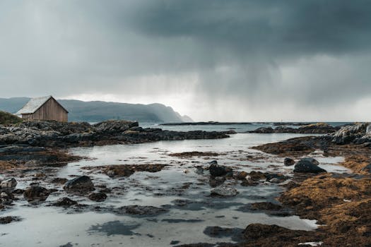 Moody view of a beach house by rocky sea cliffs under cloudy skies in Norway.