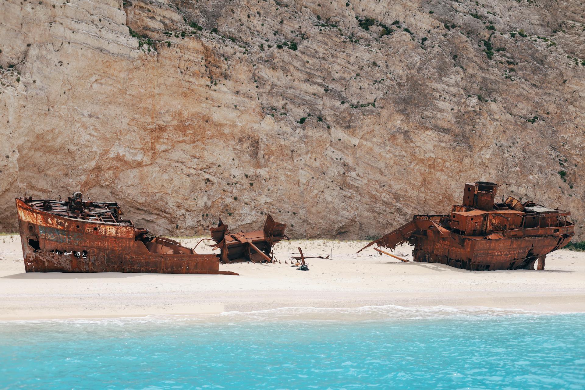 Rusted shipwrecks rest on Navagio Beach in Zakynthos, Greece, with turquoise water and rocky cliffs.
