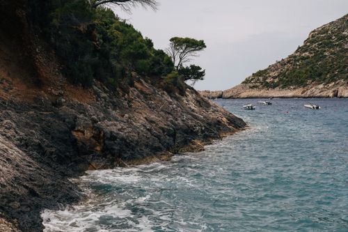 Free Serene coastal view featuring rocky cliffs, calm sea, and small boats in a Mediterranean setting. Stock Photo