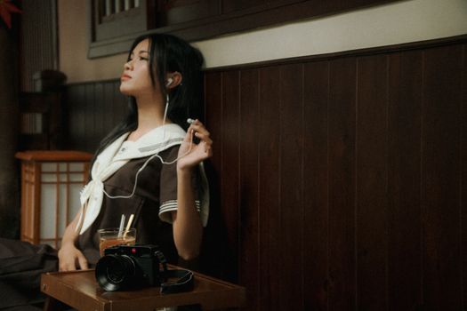 A young woman relaxes with headphones indoors, deep in thought.