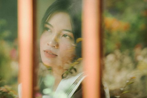 Free A thoughtful woman gazes outside through a glass window, surrounded by nature. Stock Photo