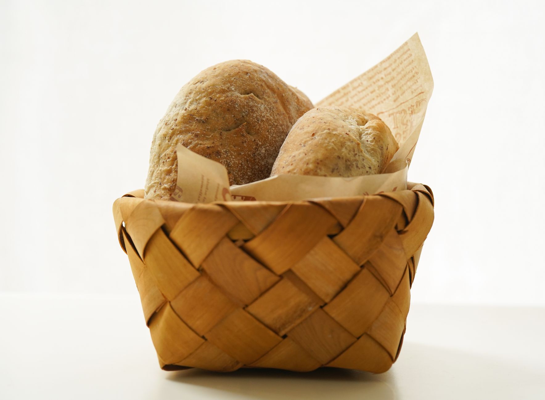 Artistic composition of fresh bread in a wicker basket with parchment paper.