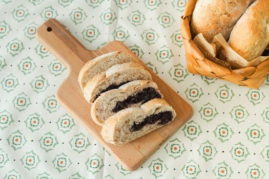A delicious variety of bread slices on a wooden cutting board beside a wicker basket of buns.