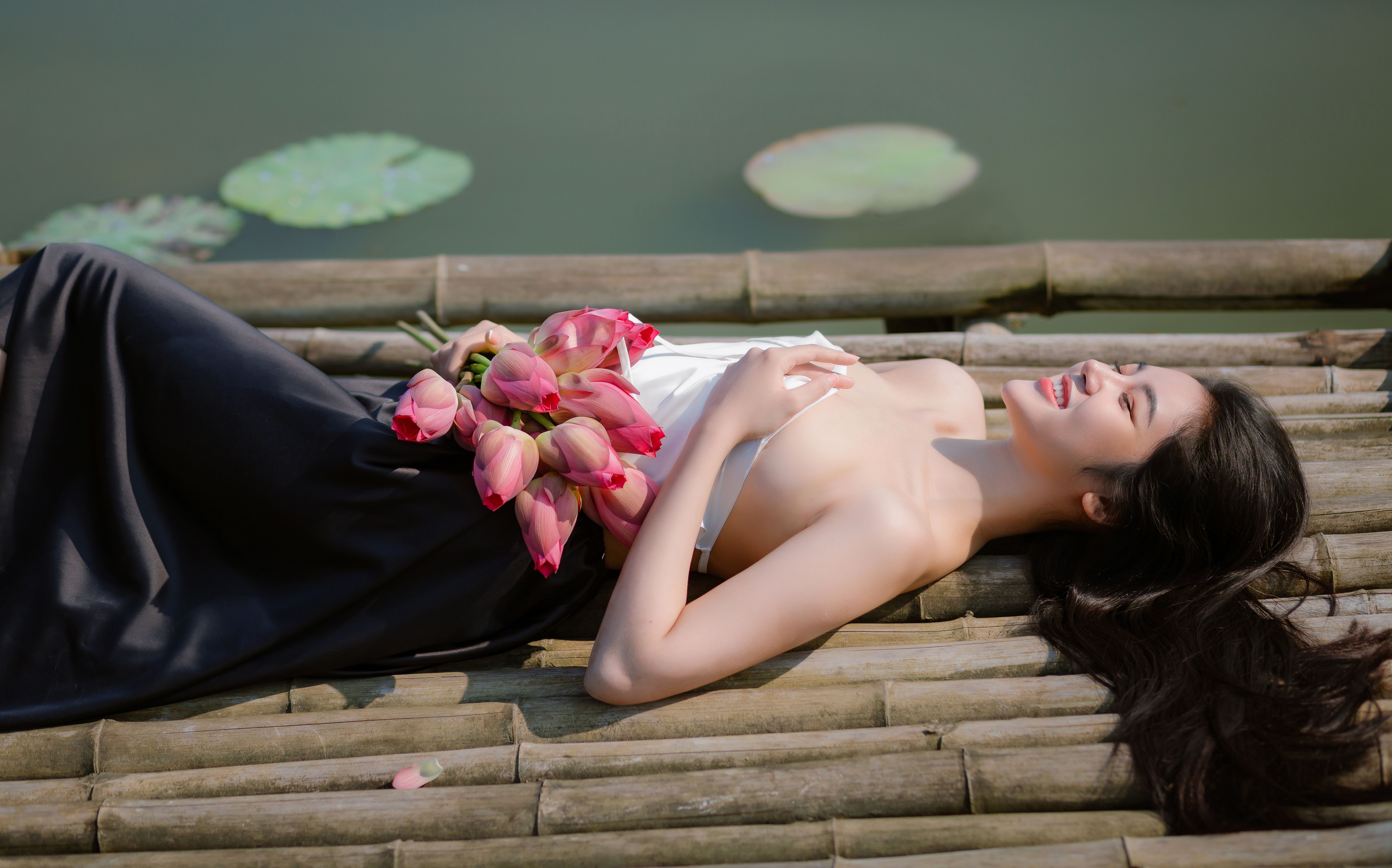 A woman lies gracefully with lotus flowers on a bamboo dock by a serene pond in Hội An.