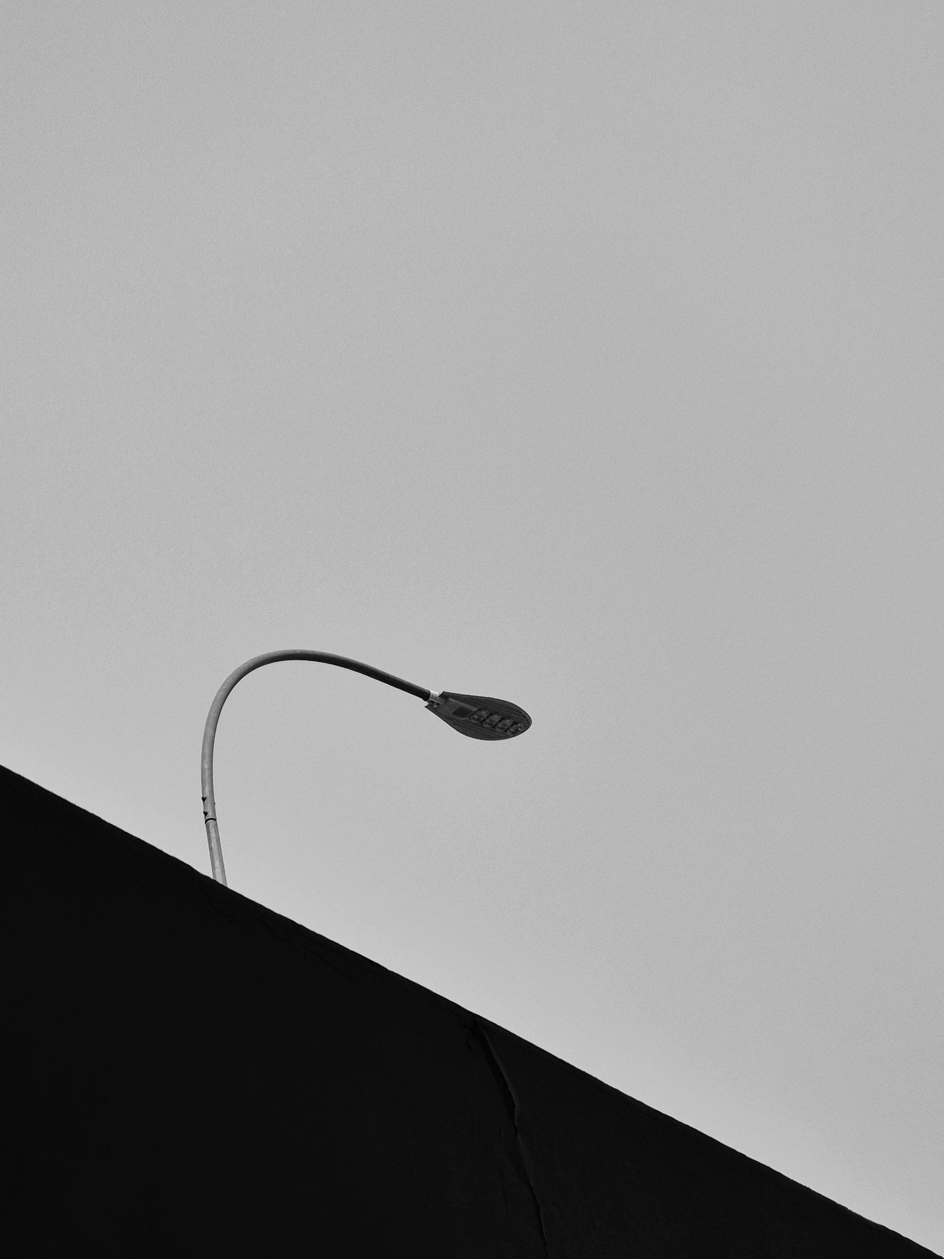 gratis Een minimalistische weergave van een lantaarnpaal tegen een grijze lucht, die de stedelijke eenvoud benadrukt. Stockfoto