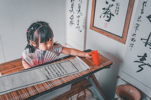 Young girl practicing calligraphy with traditional tools indoors.