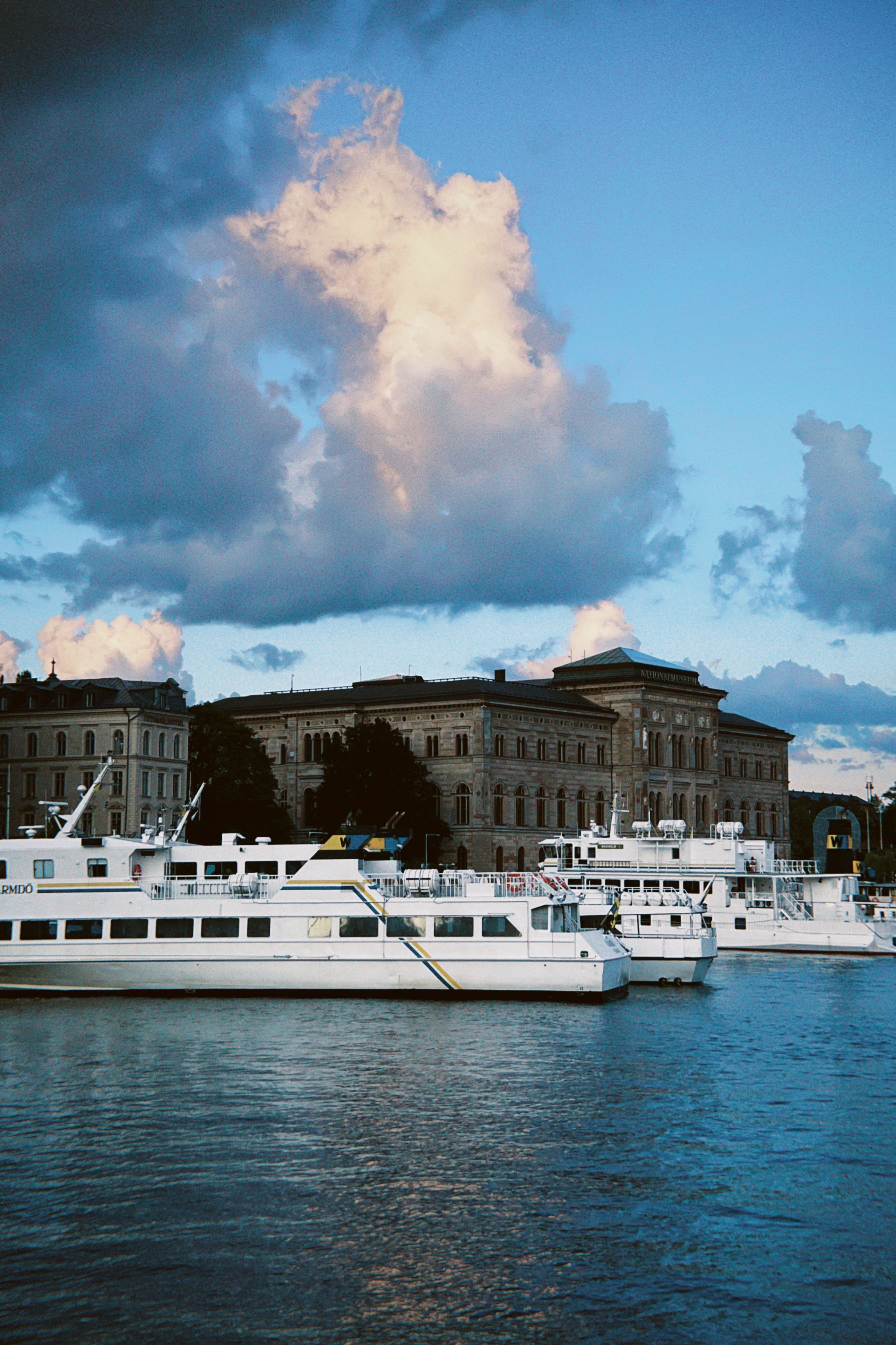 Elegant boats docked by a historic building under a vibrant sky in Stockholm.