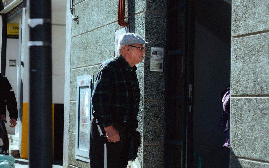 Un hombre mayor con gorra entrando en un edificio en Arganda del Rey, Madrid, en un día soleado.
