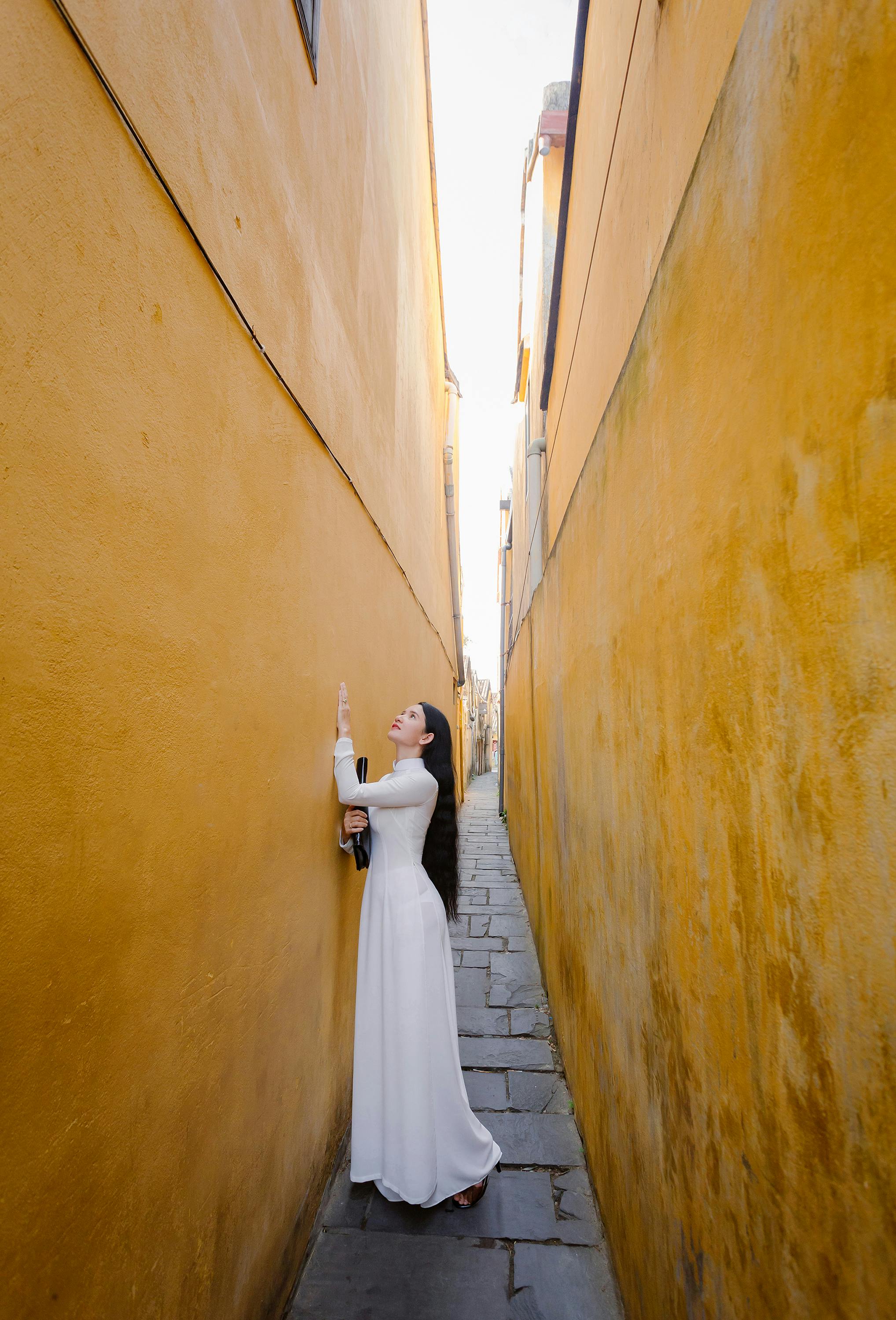 Elegant woman in traditional Ao Dai in Hoi An's narrow yellow alleyway, Vietnam.