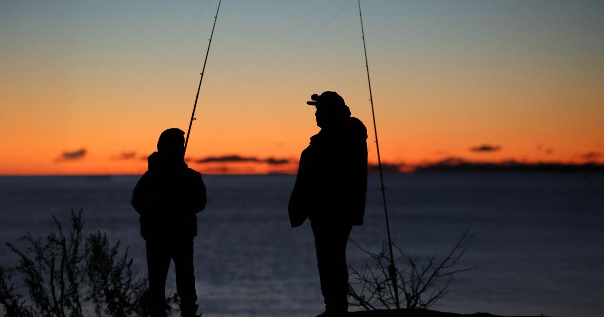 A father and son fishing together at the edge of a lake at sunrise