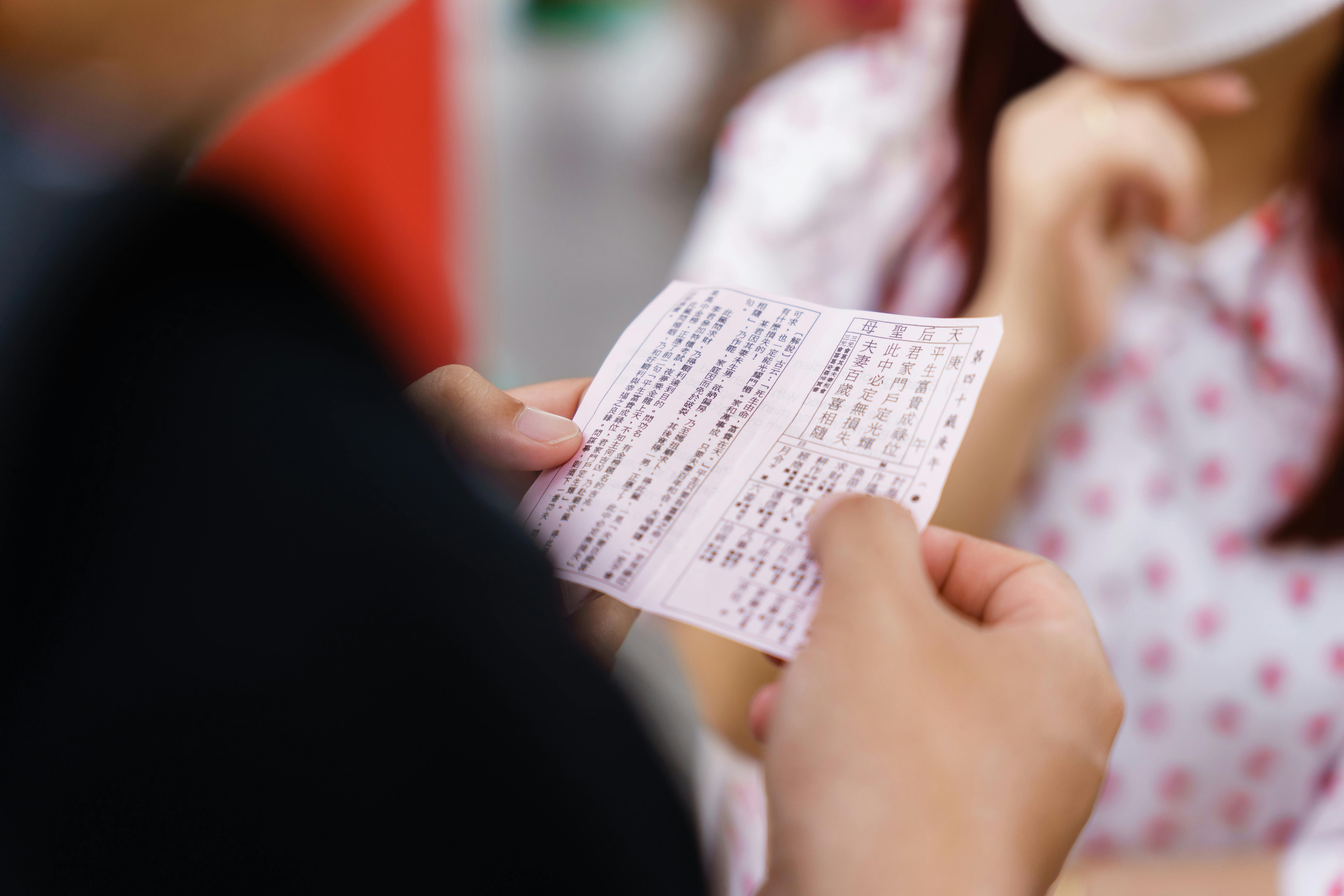 Two people interacting indoors, holding a document with Asian characters, focus on hands.