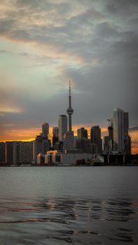 Dramatic view of Toronto skyline with CN Tower at sunset, reflecting on lake.