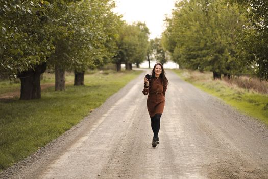 Smiling woman photographer walking with camera on a rural road lined with trees.