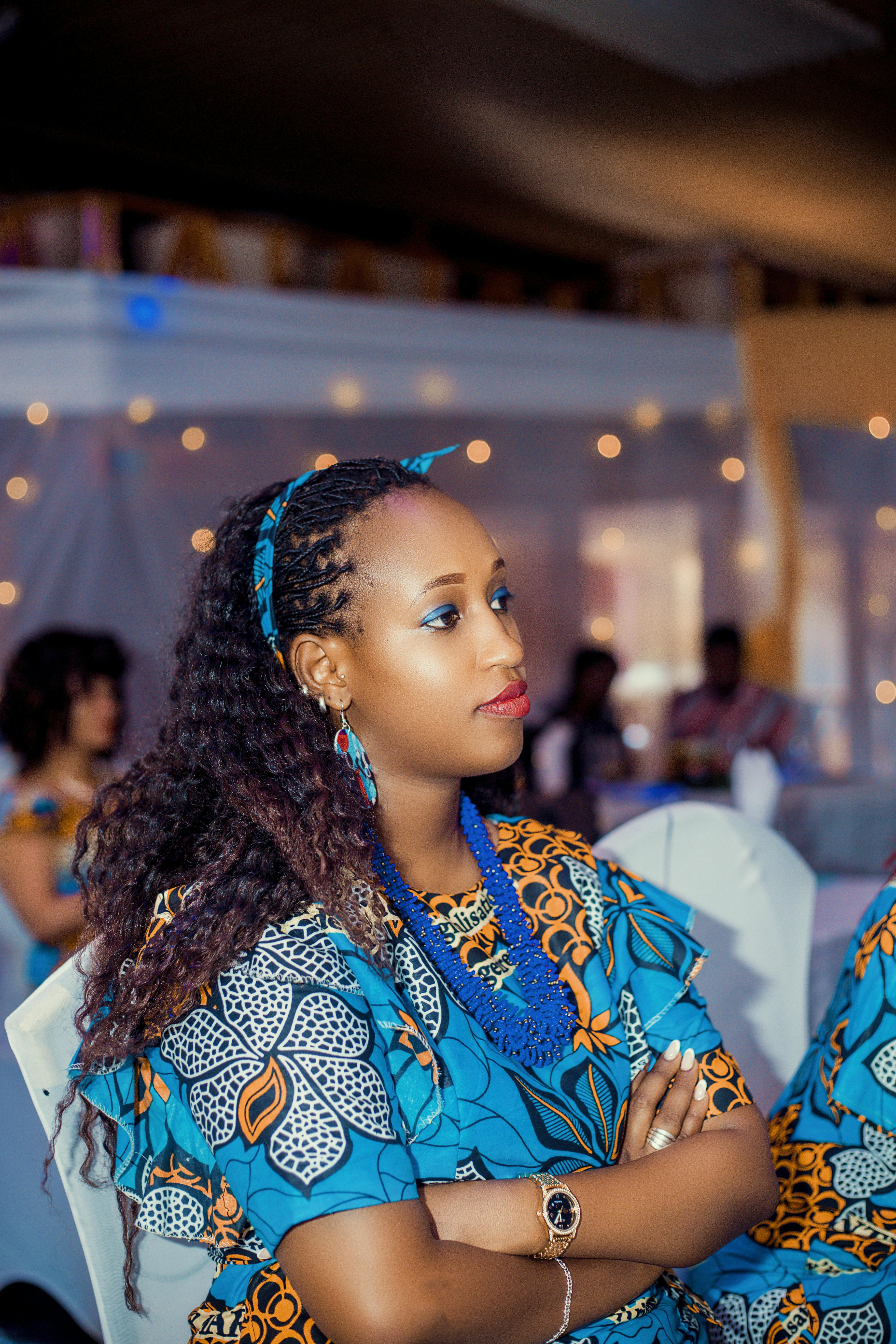 De franc Dona elegant amb vestits tradicionals africans vibrants asseguda en un esdeveniment a l'interior, amb aspecte pensatiu. Foto d'estoc