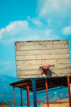 Vintage wooden basketball hoop with ball stuck, set against a clear blue sky.