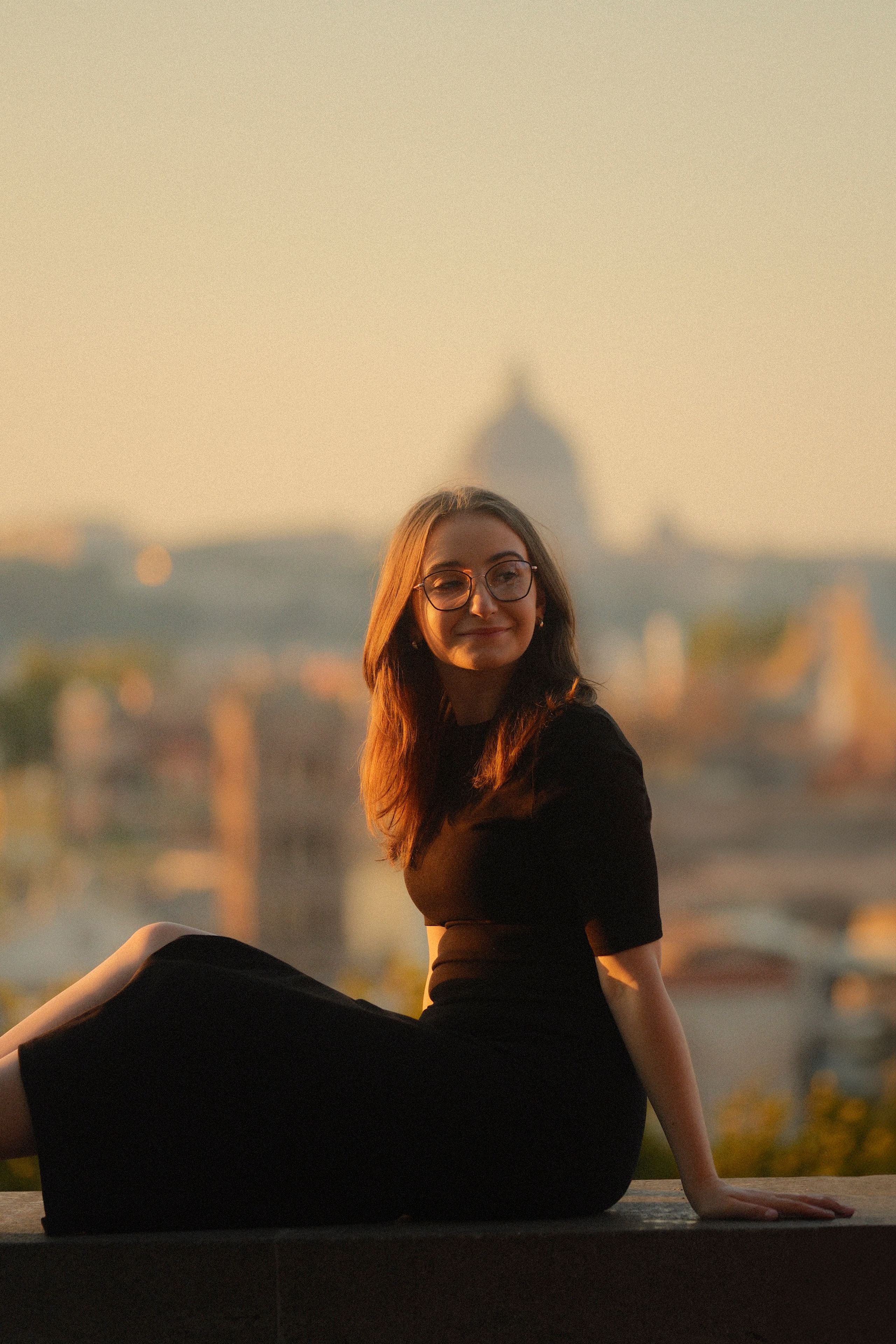 A woman enjoying a scenic view of Rome at sunset, featuring iconic architecture in soft golden light.