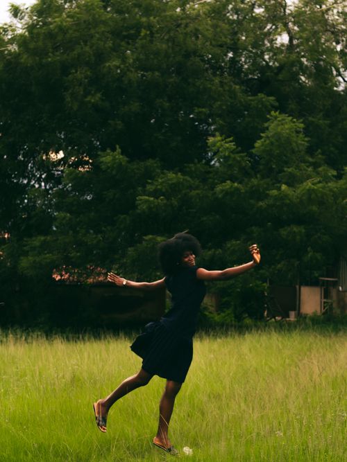 Free A woman exuberantly jumps in a lush green meadow on a sunny day, expressing freedom and joy. Stock Photo