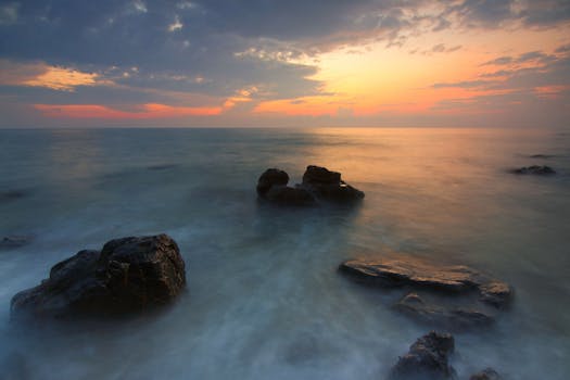 Peaceful seascape with rocks under a vibrant sunset sky, capturing the tranquil beauty of the ocean.