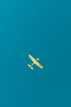 Aerial view of a classic yellow warplane flying high against a bright blue sky.