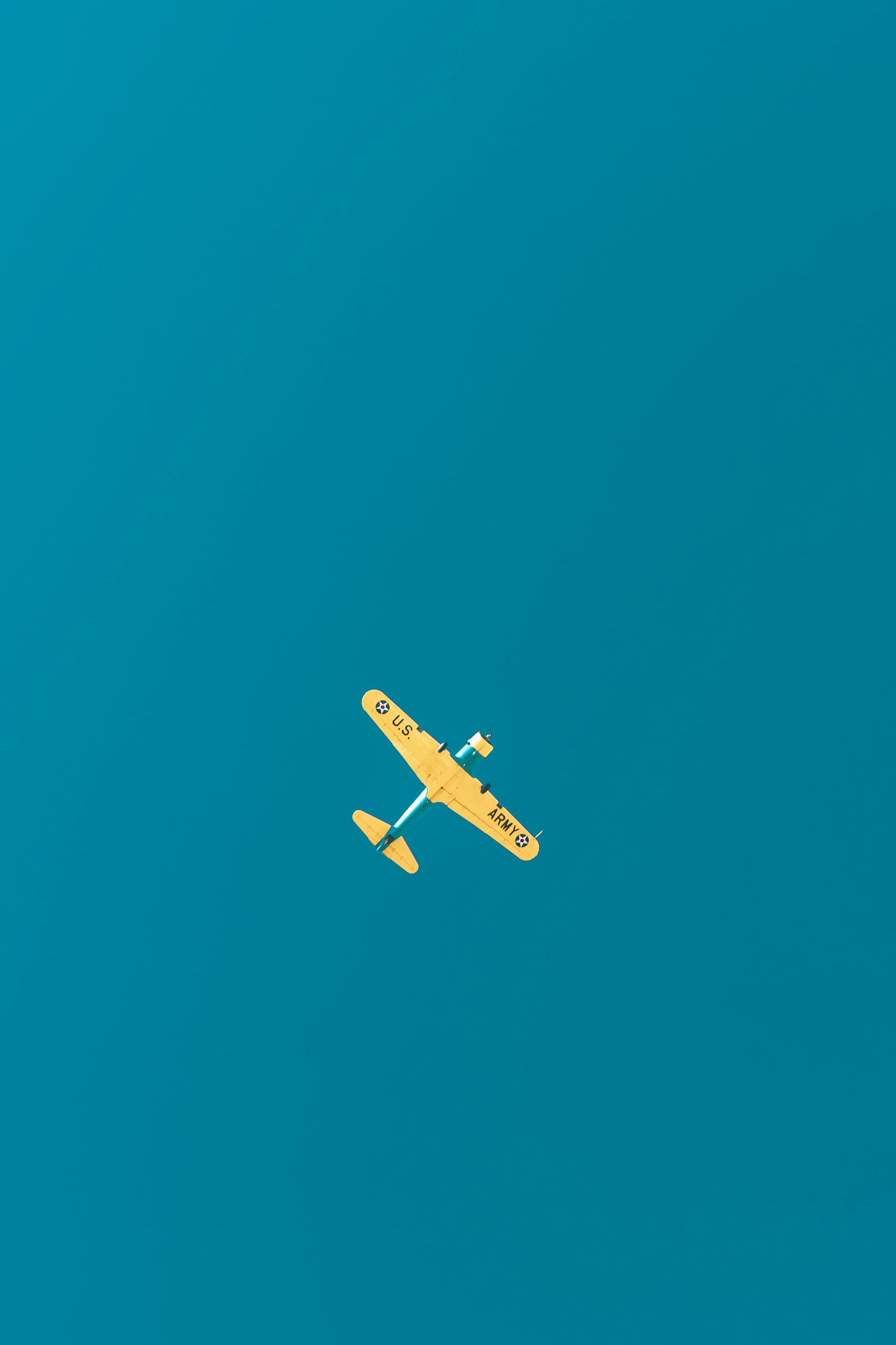 Gratis Luftfoto af et klassisk gult krigsfly, der flyver højt mod en lys blå himmel. Lagerfoto