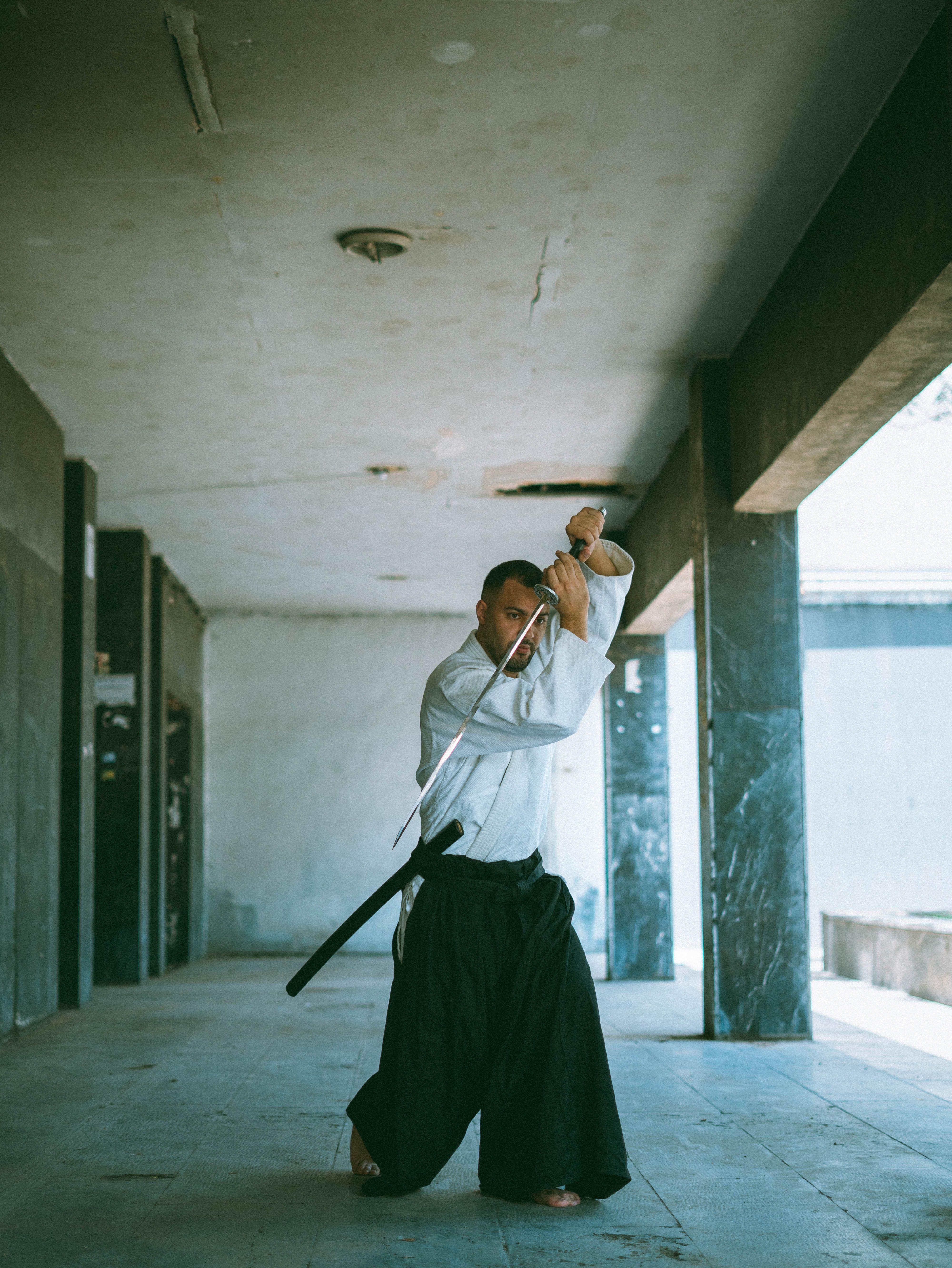 A focused martial artist practices with a katana sword in an indoor hallway, showcasing skill and discipline.