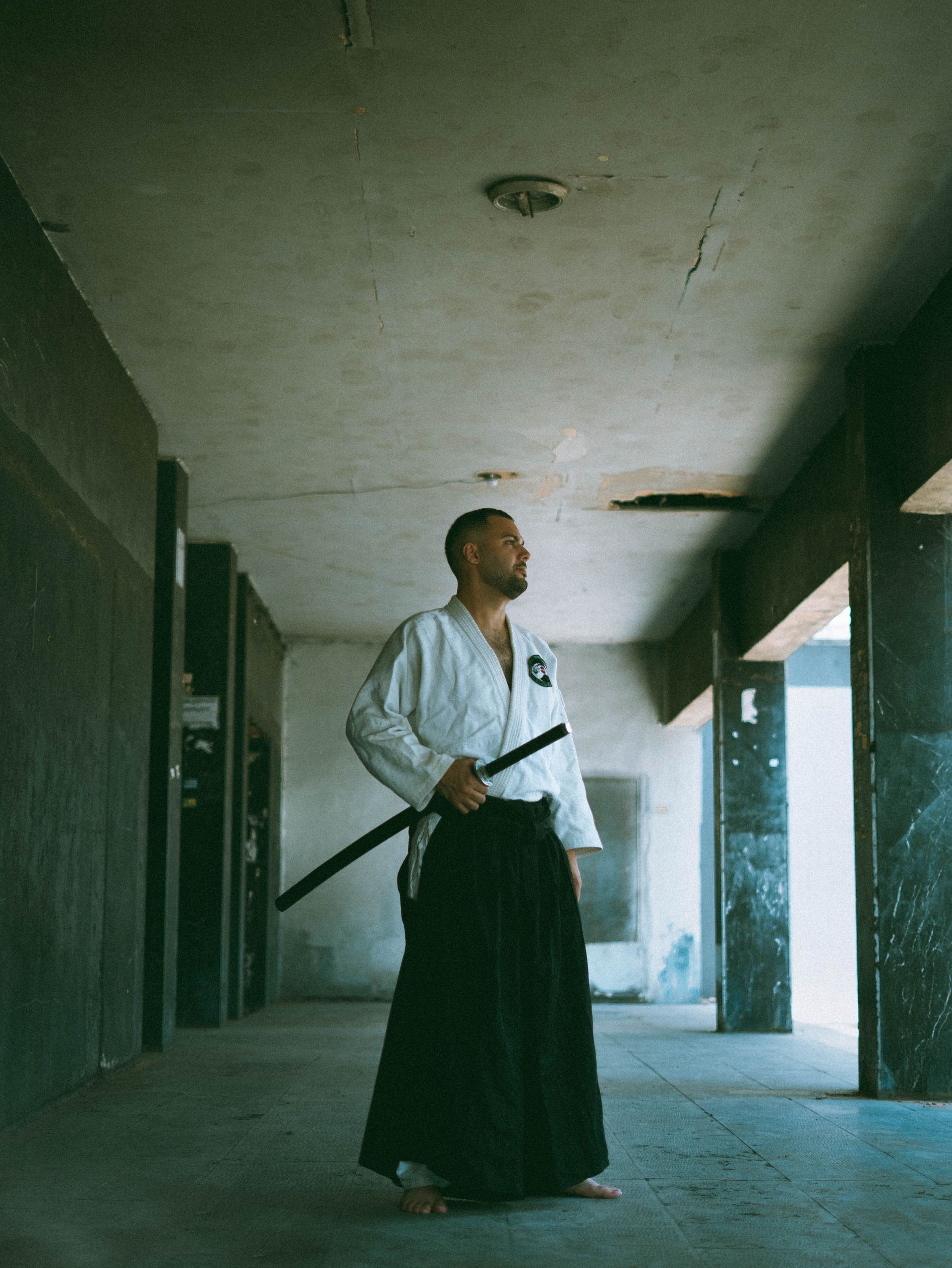 Black and white photograph of a martial artist practicing Iaido, holding a katana in a dim corridor