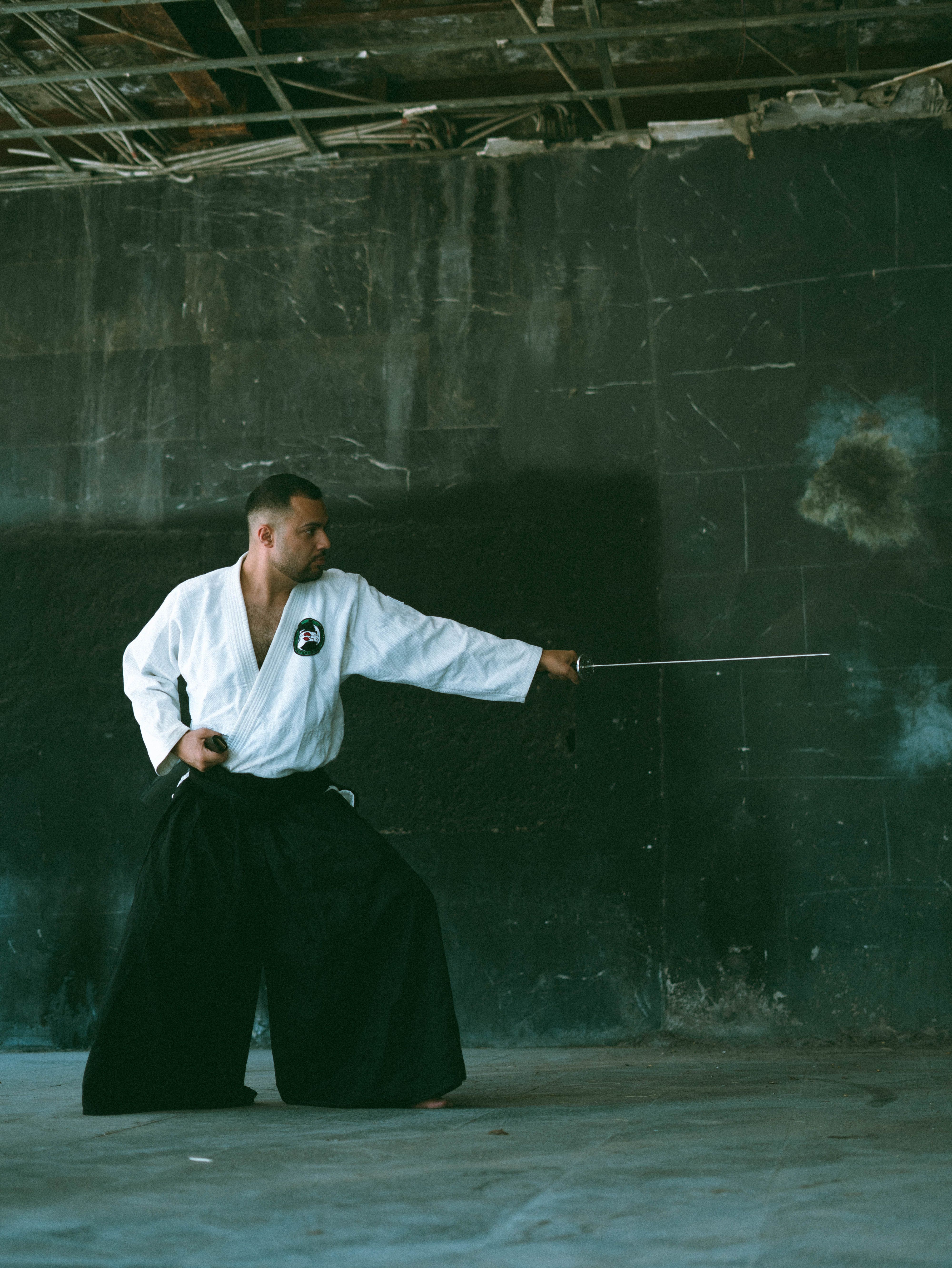Martial artist in traditional attire practicing katana techniques in an urban indoor setting.