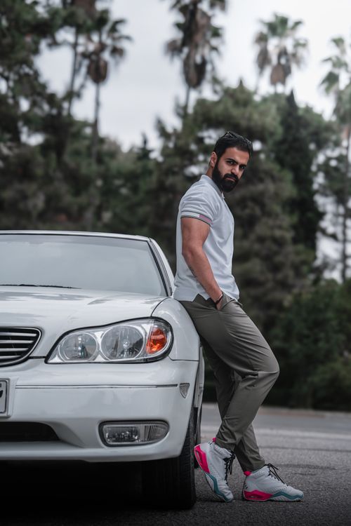 Free Man in casual attire leaning on car with palm trees in background. Stock Photo