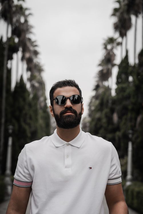 Free Confident man wearing sunglasses on a palm-lined path. Stock Photo