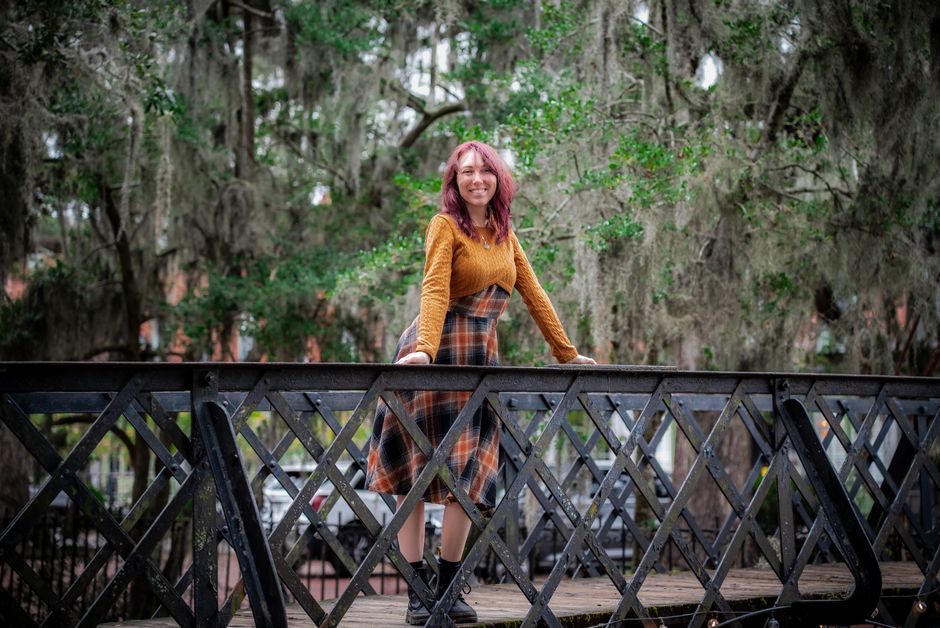 A woman stands confidently on a bridge surrounded by lush greenery in Savannah, Georgia.