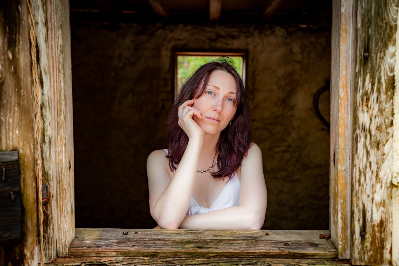 woman in white top leaning on rustic window sill outdoors natural ligh