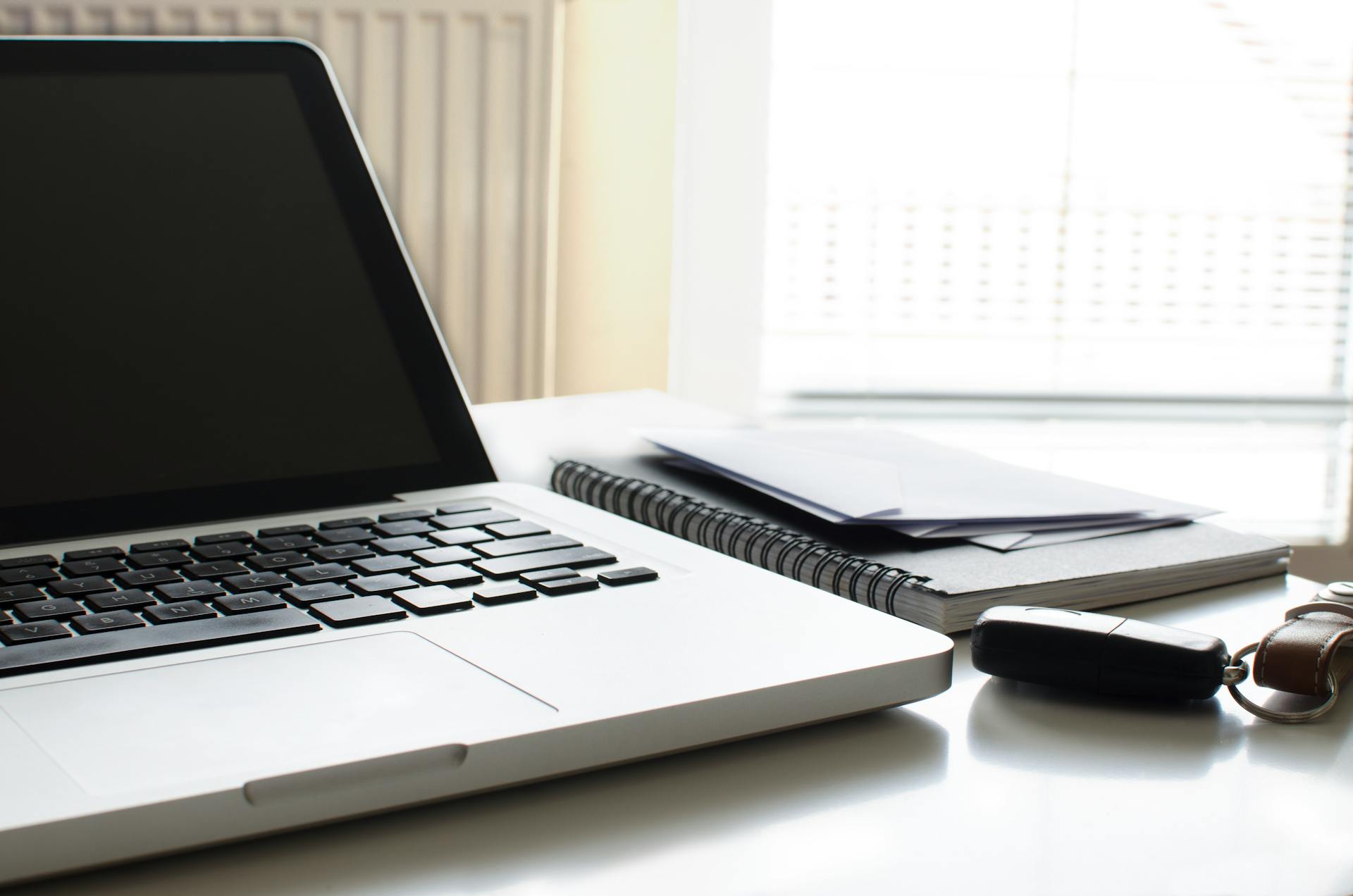 Contemporary office setup featuring a laptop, notebook, envelopes, and car keys on a desk.