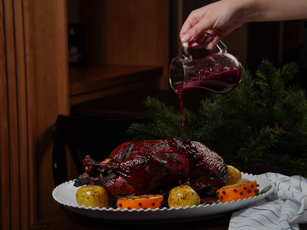 Gratis Un hermoso pato asado con salsa de arándanos, acompañado de frutas decoradas para una comida festiva. Foto de stock