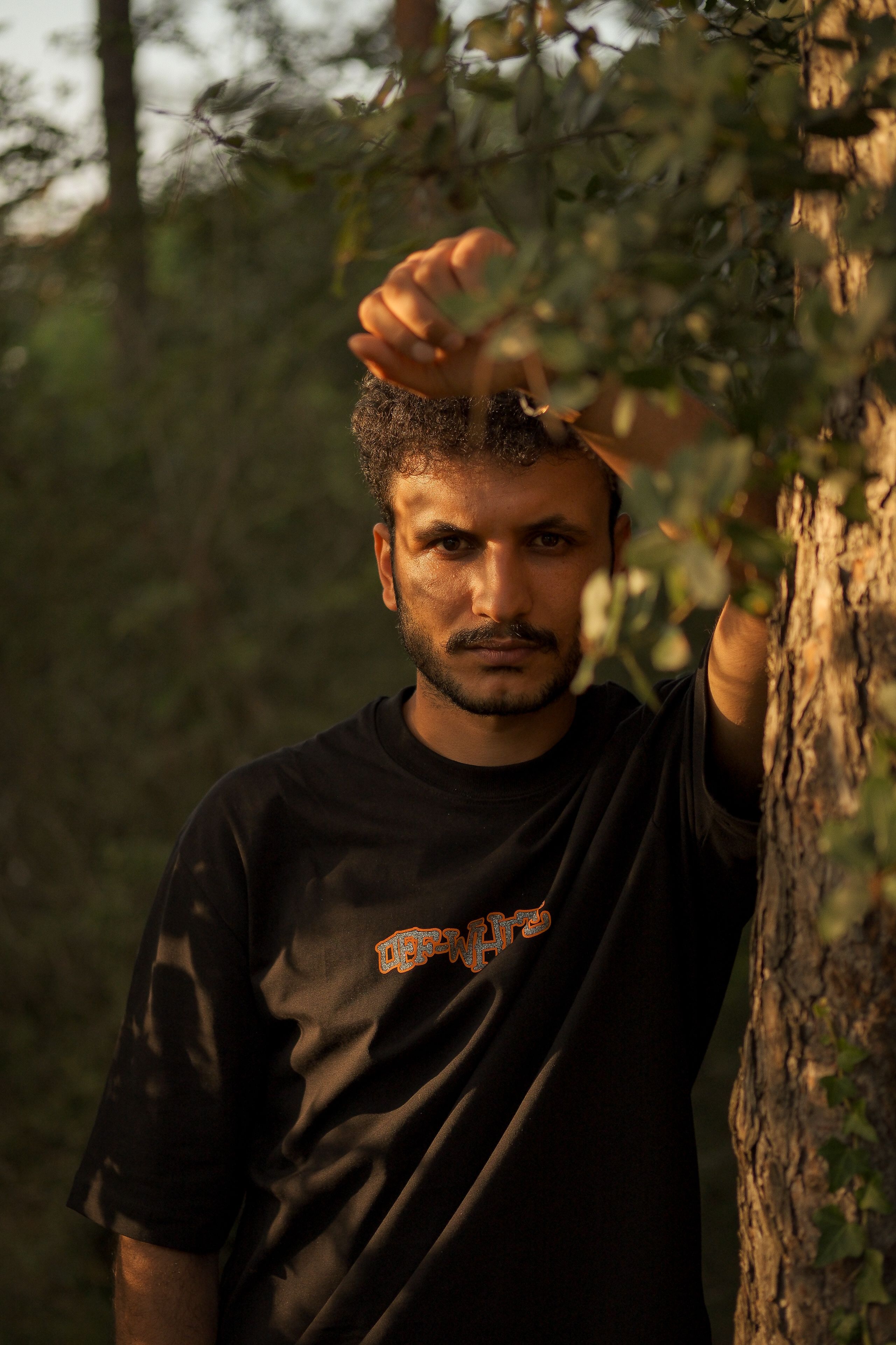Contemplative portrait of a man leaning on a tree in a forest.